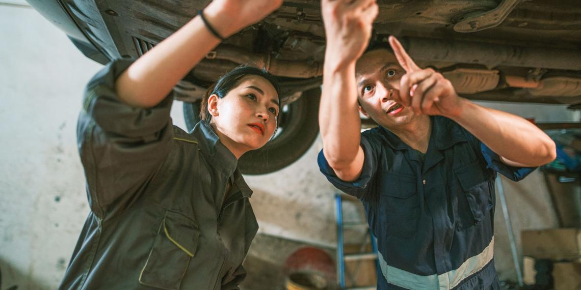 Student and teacher work underneath a car